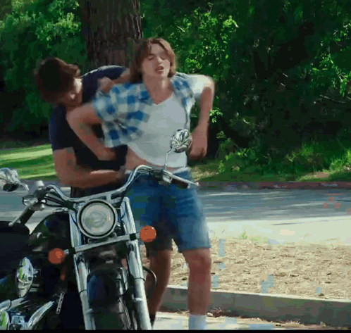 A Man Is Holding Another Man 'S Waist While Riding A Motorcycle GIF