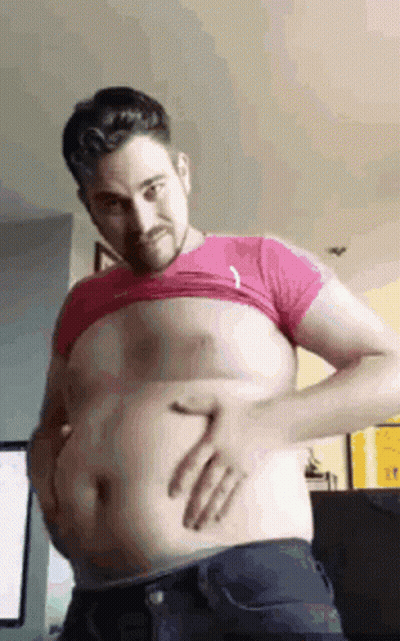 A Man Is Holding His Belly With His Hands While Wearing A Pink Shirt . GIF