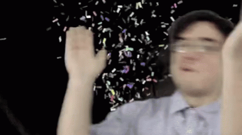 A Man Is Holding His Hands Up In The Air While Confetti Is Falling From The Sky . GIF