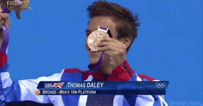 A Man Is Holding Up A Gold Medal With The Name Thomas Daley On The Bottom GIF