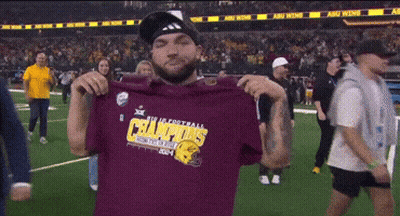 A Man Is Holding Up A Shirt That Says Champions On It GIF