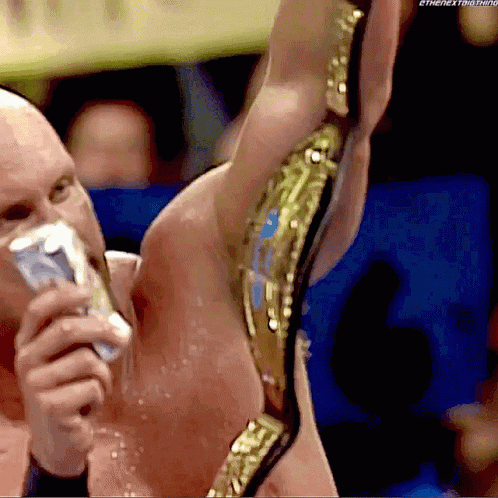 A Man Is Holding Up A Wrestling Belt While Drinking From A Bottle GIF