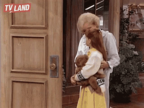 A Man Is Hugging A Little Girl Who Is Holding A Teddy Bear In Front Of A Wooden Door . GIF