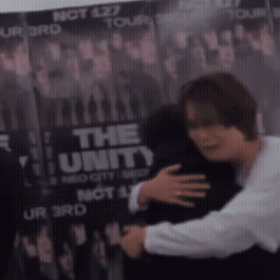 A Man Is Hugging Another Man In Front Of A Poster That Says The Unity GIF