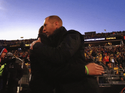 A Man Is Hugging Another Man In Front Of A Sign That Says " Starting N " GIF
