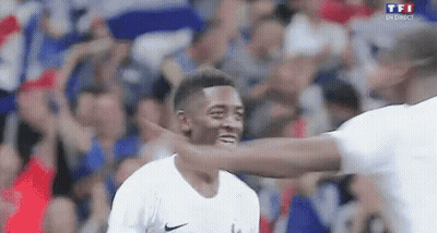 A Man Is Hugging Another Man On A Soccer Field While A Crowd Watches . GIF