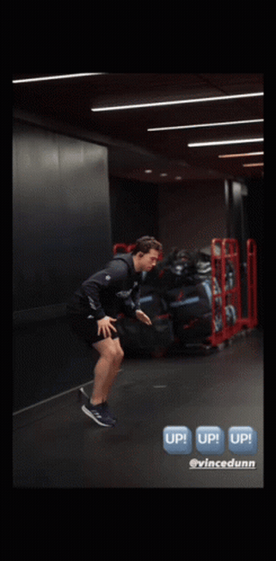 A Man Is Jumping In The Air In A Gym With A Sign That Says Up GIF