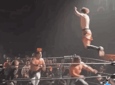 A Man Is Jumping In The Air In A Wrestling Ring With An Exit Sign Behind Him GIF