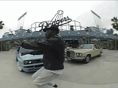 A Man Is Jumping In The Air In Front Of Dodgers Stadium GIF