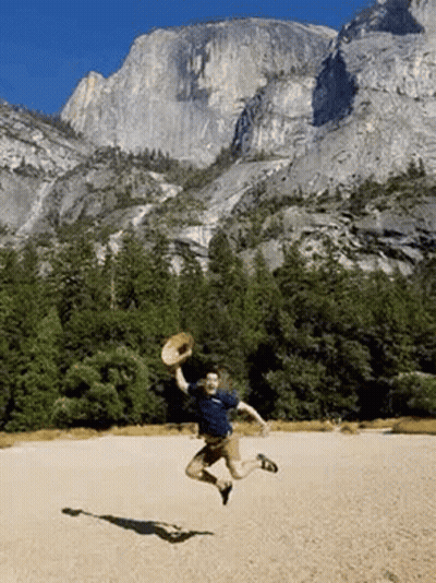 A Man Is Jumping In The Air While Holding A Straw Hat . GIF