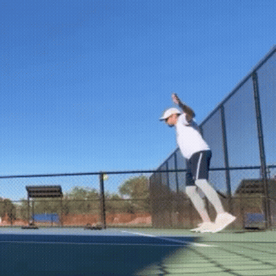 A Man Is Jumping In The Air While Holding A Tennis Racquet On A Tennis Court . GIF