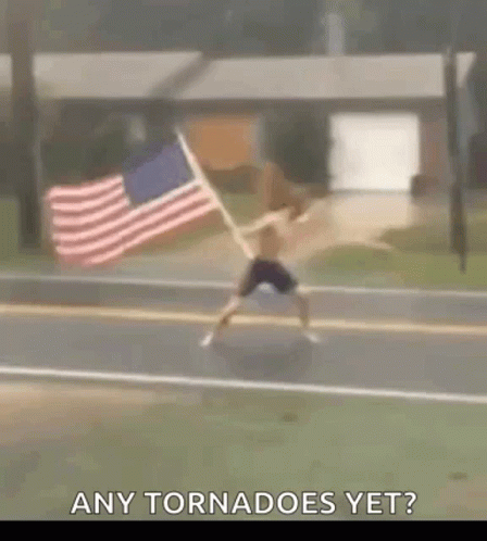 A Man Is Jumping In The Air While Holding An American Flag On The Side Of The Road . GIF
