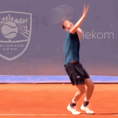 A Man Is Jumping In The Air While Playing Tennis In Front Of A Belgrade Open Sign GIF