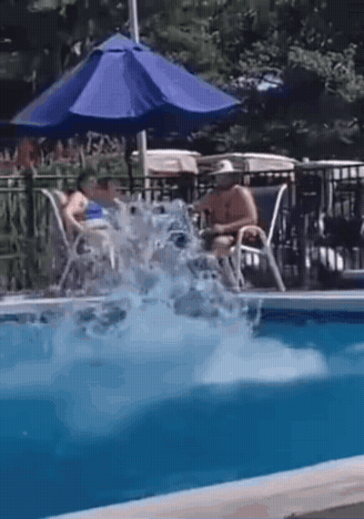 A Man Is Jumping Into A Swimming Pool While A Woman Sits On A Chair Under An Umbrella . GIF