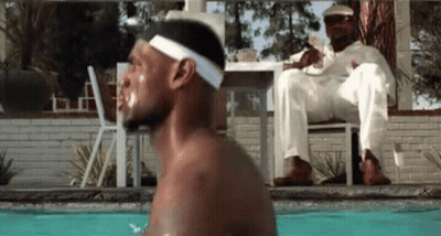 A Man Is Jumping Into A Swimming Pool While Another Man Sits On A Chair . GIF