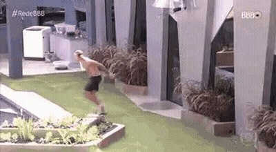 A Man Is Jumping Into A Swimming Pool While Wearing Shorts . GIF