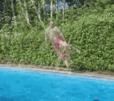 A Man Is Jumping Into A Swimming Pool With Trees In The Background . GIF