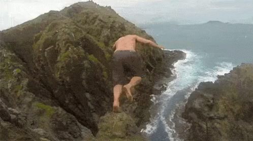 A Man Is Jumping Off A Rock Into The Ocean . GIF