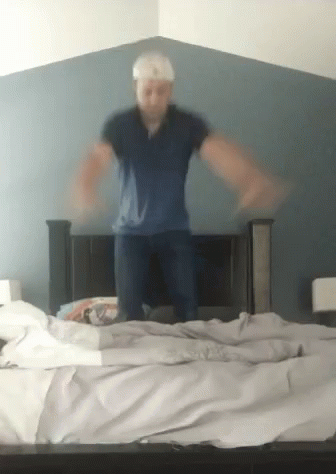 A Man Is Jumping On A Bed In A Bedroom GIF