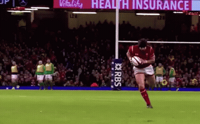 A Man Is Kicking A Rugby Ball On A Field With A Sign That Says Health Insurance In The Background . GIF
