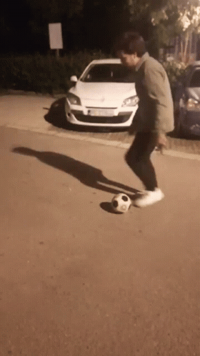 A Man Is Kicking A Soccer Ball On The Sidewalk In Front Of A White Car GIF