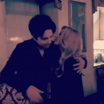 A Man Is Kissing A Woman On The Cheek In A Living Room . GIF
