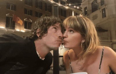 A Man Is Kissing A Woman On The Cheek In Front Of A Building GIF
