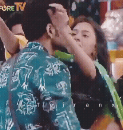 A Man Is Kissing A Woman On The Cheek In Front Of A Fore Tv Sign GIF