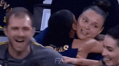 A Man Is Kissing A Woman On The Cheek While Sitting In A Basketball Stadium . GIF