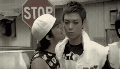 A Man Is Kissing Another Man On The Cheek While Standing In Front Of A Stop Sign . GIF
