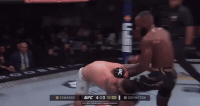 A Man Is Kneeling Down In A Boxing Ring While Another Man Kicks Him . GIF