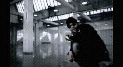 A Man Is Kneeling Down In A Dark Room With A Gun . GIF