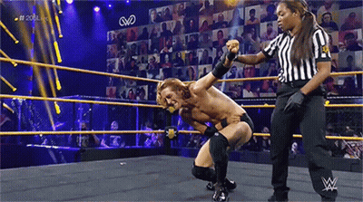 A Man Is Kneeling Down In A Wrestling Ring With A Referee Standing Behind Him . GIF