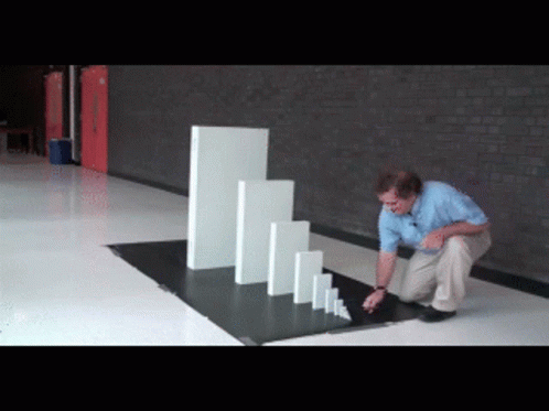 A Man Is Kneeling Down In Front Of A Row Of Dominoes GIF