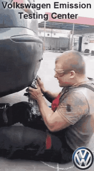 A Man Is Kneeling Down In Front Of A Volkswagen Car . GIF