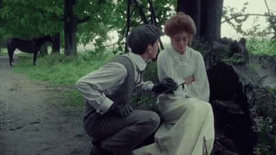 A Man Is Kneeling Down Next To A Woman Sitting On A Bench With A Horse In The Background . GIF