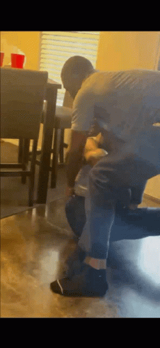 A Man Is Kneeling Down Next To Another Man In A Living Room While Holding A Bottle Of Water . GIF