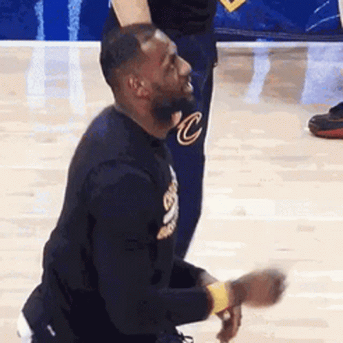 A Man Is Kneeling Down On A Basketball Court With His Hands In His Pockets . GIF
