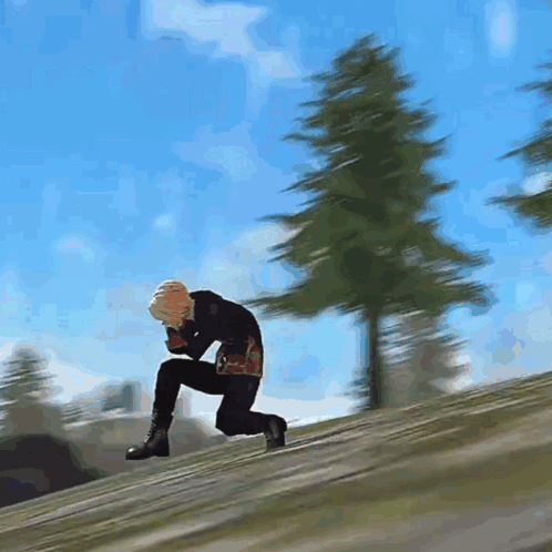 A Man Is Kneeling Down On A Hill With Trees In The Background GIF