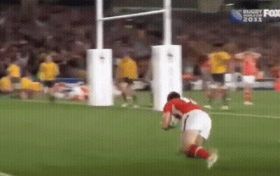 A Man Is Kneeling Down On A Soccer Field With A Rugby Ball . GIF