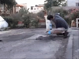 A Man Is Kneeling Down On The Sidewalk With A Bottle Of Water In Front Of Him GIF