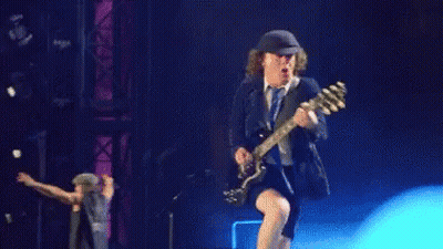 A Man Is Kneeling Down While Playing A Guitar On Stage . GIF