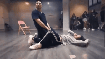 A Man Is Kneeling Over A Woman Laying On The Floor In A Dance Studio . GIF