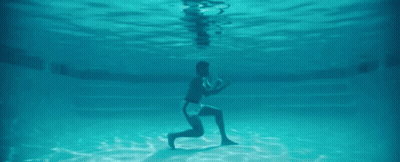 A Man Is Kneeling Underwater In A Swimming Pool . GIF