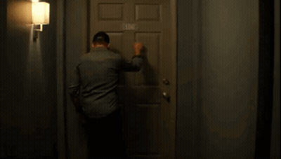 A Man Is Knocking On A Door In A Hallway . GIF