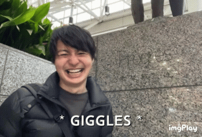 A Man Is Laughing In Front Of A Stone Wall And The Word Giggles Is Above Him GIF