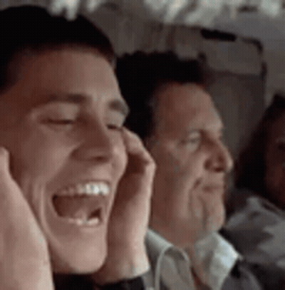 A Man Is Laughing On A Plane While Another Man Covers His Ears . GIF