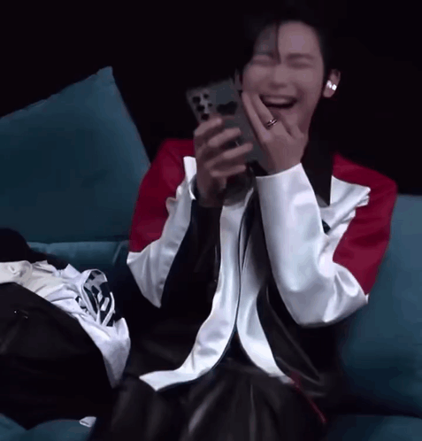 A Man Is Laughing While Holding A Cell Phone In His Hand GIF