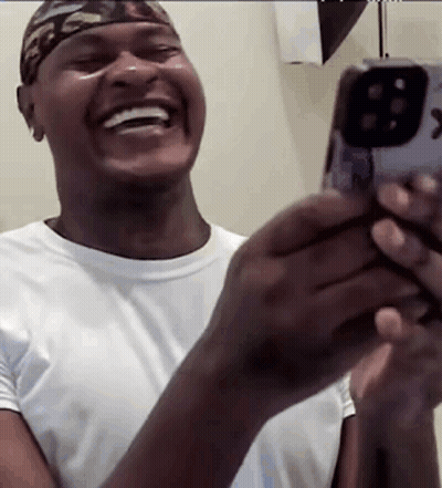 A Man Is Laughing While Holding A Cell Phone In His Hands . GIF