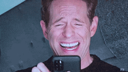 A Man Is Laughing While Looking At His Phone With Fx On The Bottom Right GIF